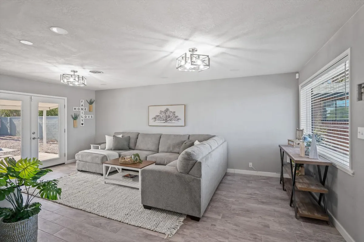 A spacious and inviting living room featuring a gray sectional sofa, coffee table, lush indoor plant, tasteful wall art, and a side table. The space is styled for comfort, with soft lighting and thoughtful decor that suggests a welcoming environment for both relaxation and casual gatherings.