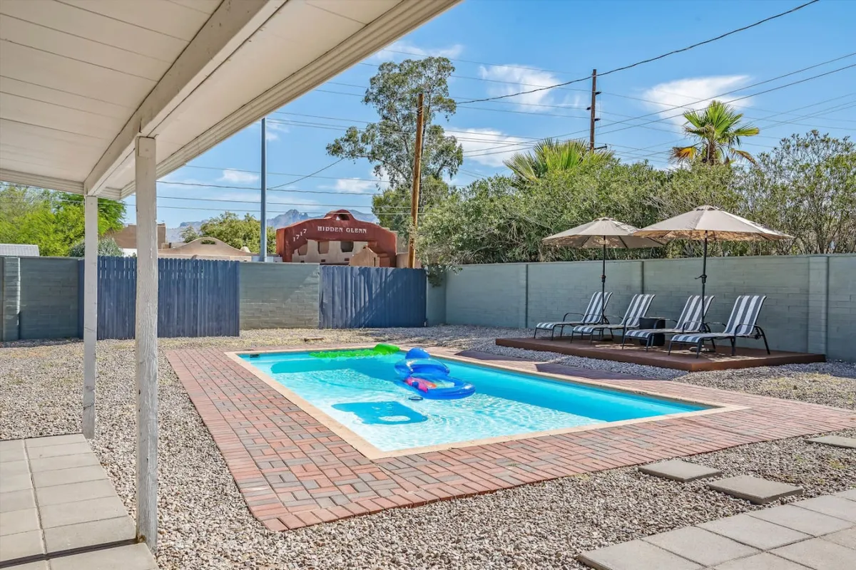 A bright pool scene with lounge chairs and umbrellas set up around the sparkling water. The mood is joyful and refreshing, with space for swimming, sunbathing, and relaxing outdoors. The arrangement reflects a welcoming atmosphere for both group activities and quiet moments.