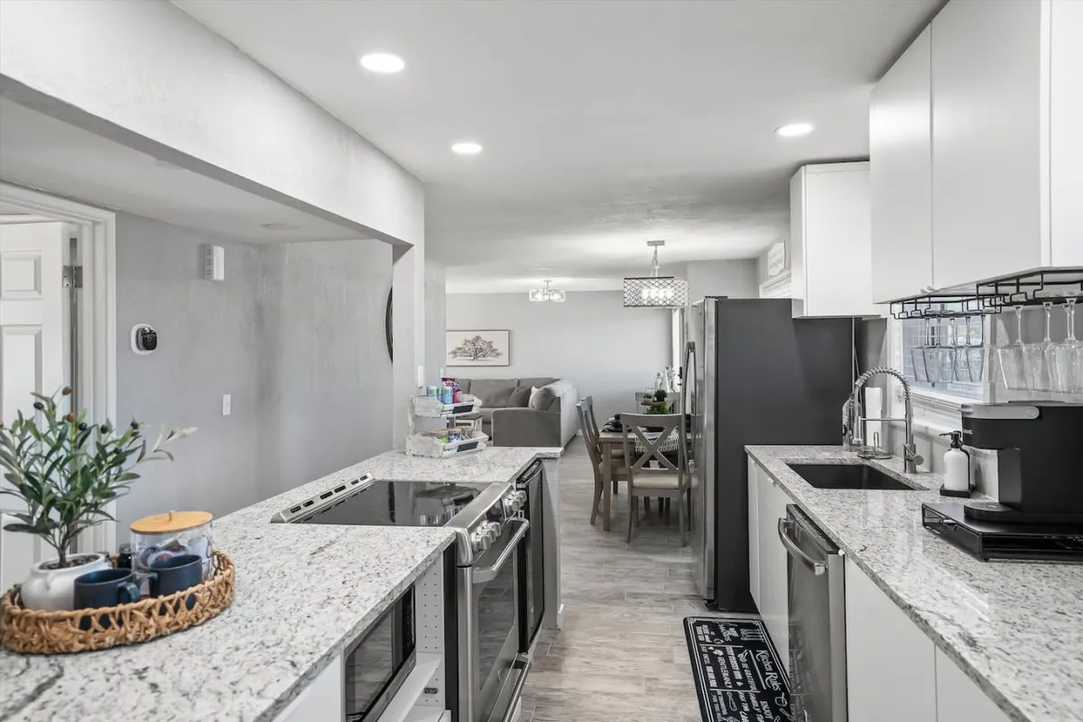 The photo focuses on a stylish granite countertop with stainless steel appliances, seamlessly connecting to a visible dining area in the background. The space feels welcoming and functional, ideal for cooking, entertaining, and sharing meals together. The composition emphasizes both the kitchen's capabilities and its role as a social hub.