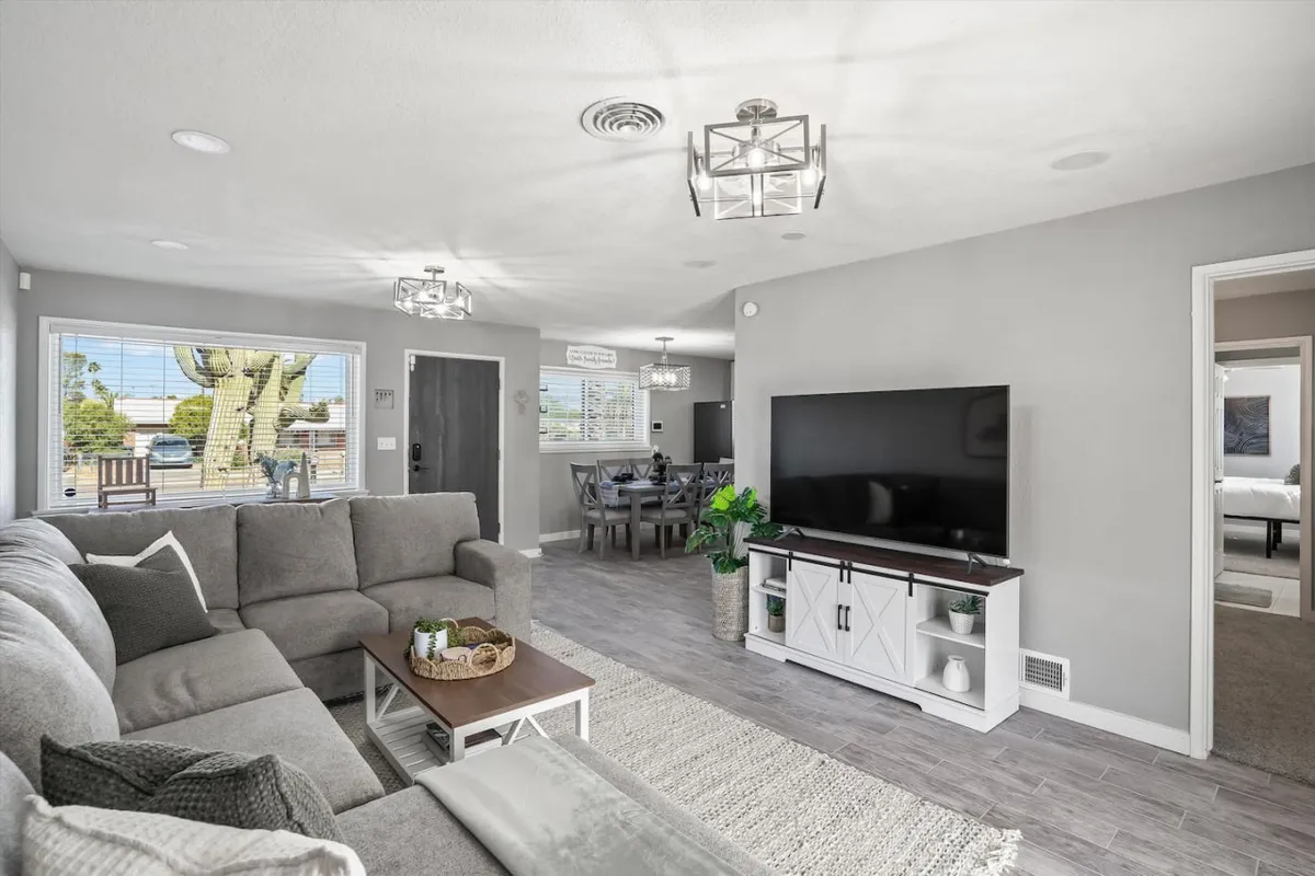 A cozy living room scene featuring a plush sofa, television, adjacent dining area, and a window offering a pleasant view. The space is organized for relaxation, socializing, and family activities such as movie nights or board games.