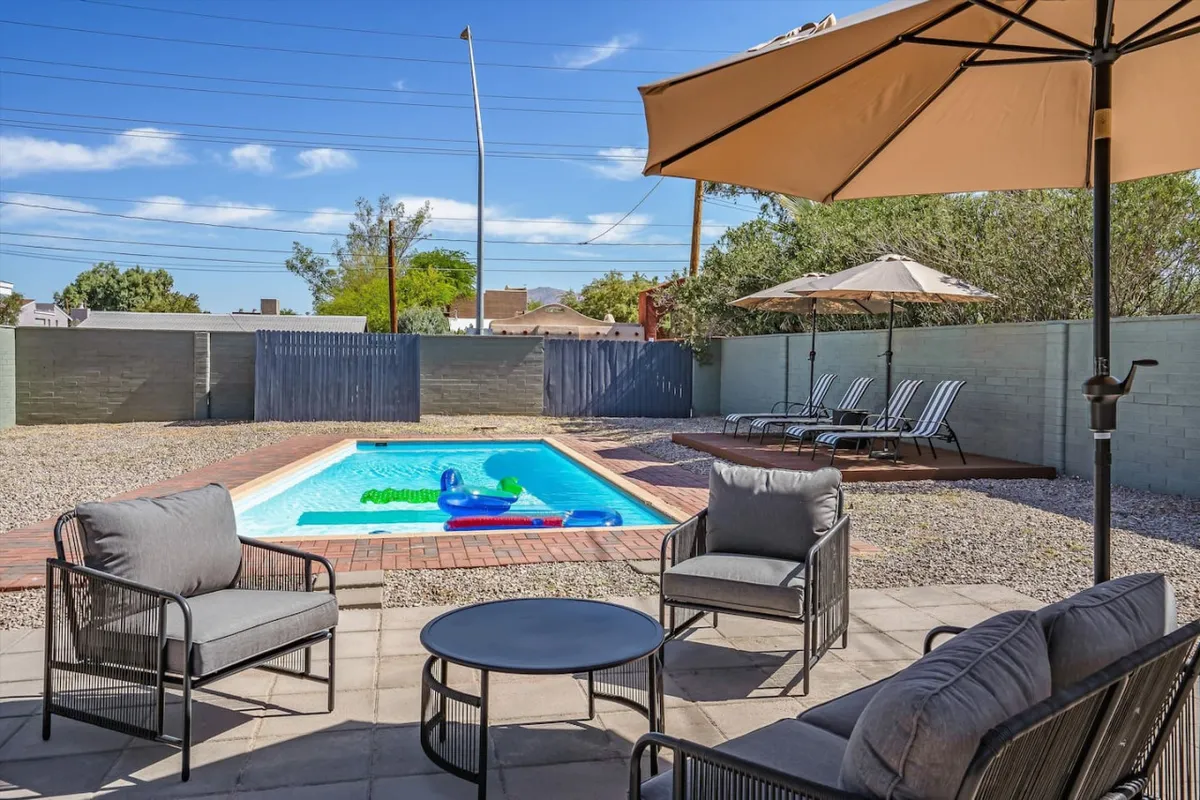 A sparkling swimming pool surrounded by an outdoor seating area and umbrella, complete with a pool float, invites guests to relax and socialize. The area is perfect for group gatherings, sunbathing, and enjoying Tucson's sunny weather.