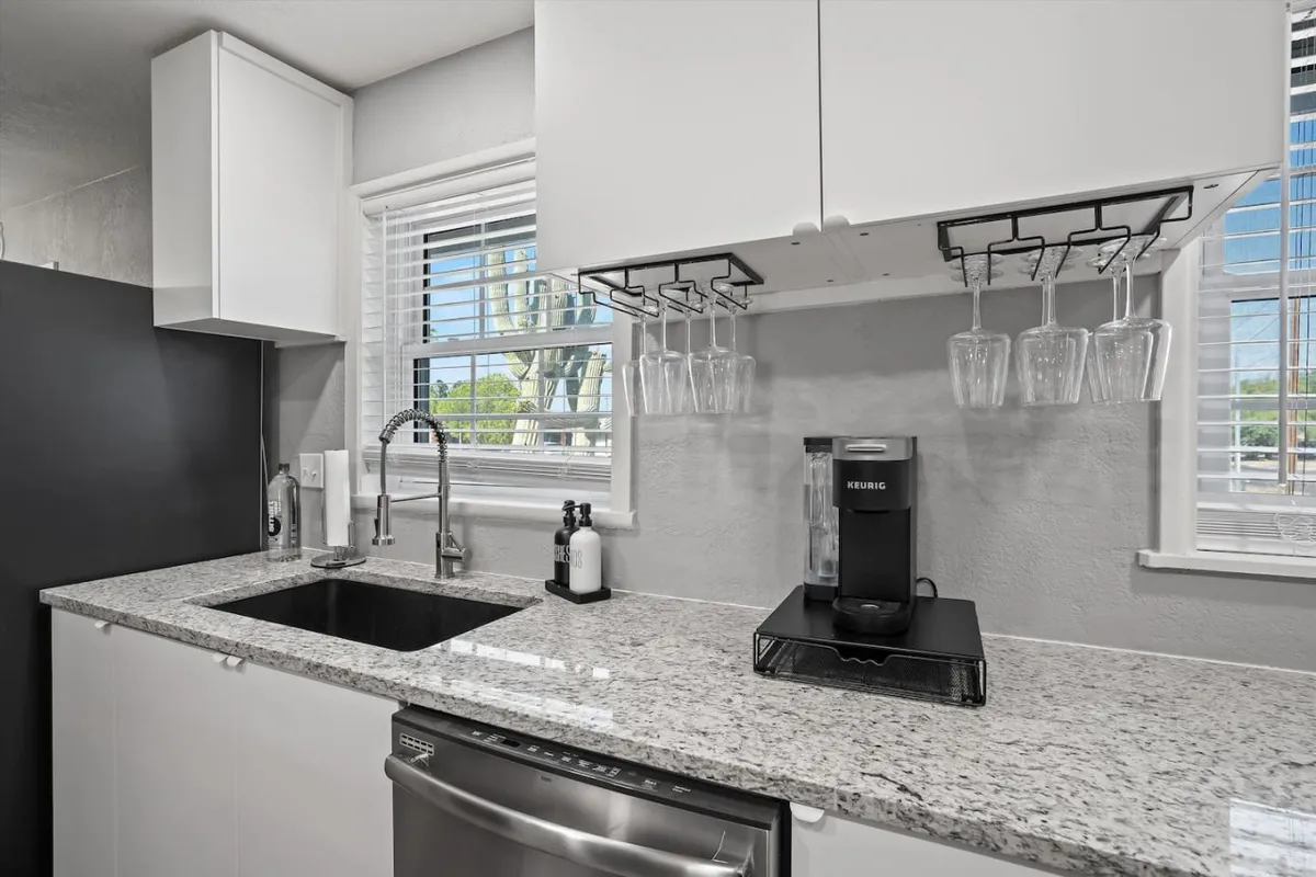 A contemporary kitchen vignette featuring a sleek granite countertop, a coffee maker set up for the morning ritual, and glassware hanging above. The space is tidy and functional, emphasizing the practical aspects of daily kitchen use, such as preparing coffee or casual meals with ease.