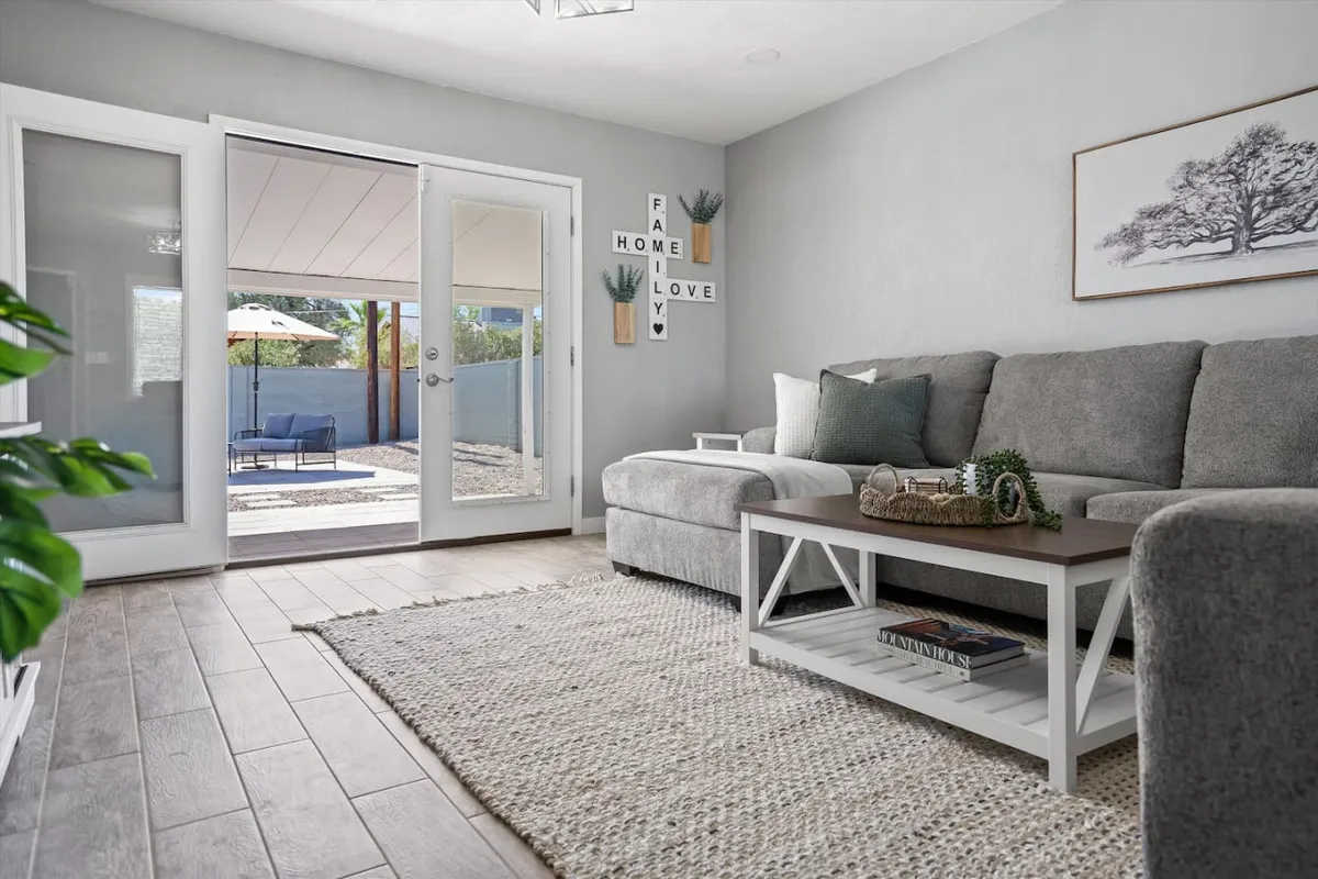 A comfortable grey sofa sits in a welcoming living space, complemented by decorative wall art, plants, and a view outside through large glass doors. The scene captures a bright, airy atmosphere that blends indoor comfort with a connection to the outdoors, hinting at easy access for exploration.